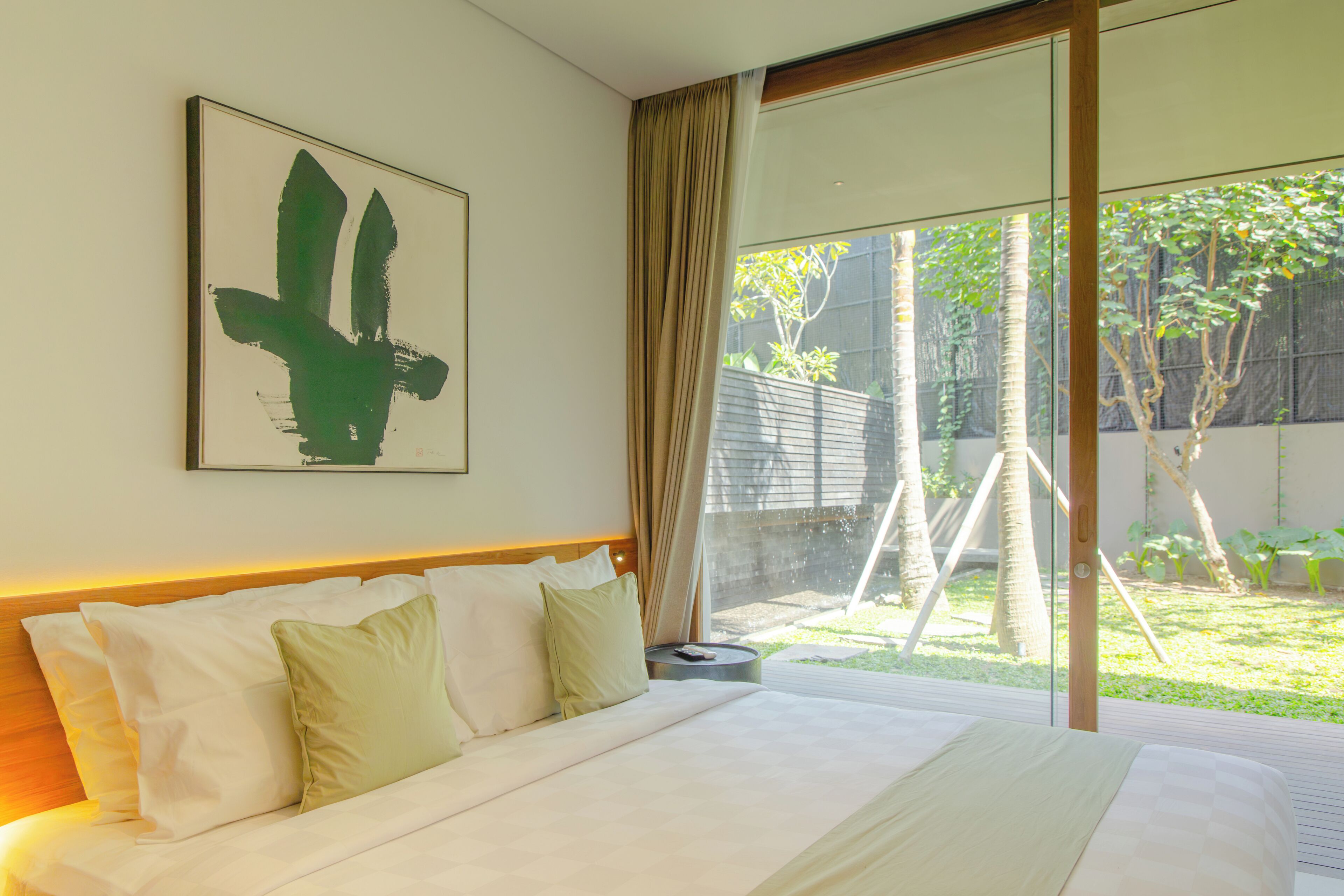 A hotel room with a large bed, a view of the garden through the window, and a framed artwork on the wall.