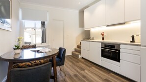 Une cuisine moderne avec des armoires blanches, un four encastré et un coin repas comprenant une table ronde et des chaises.