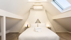 Une chambre à coucher comprenant un lit, des tables de chevet, une lampe, une fenêtre et un climatiseur intégré.