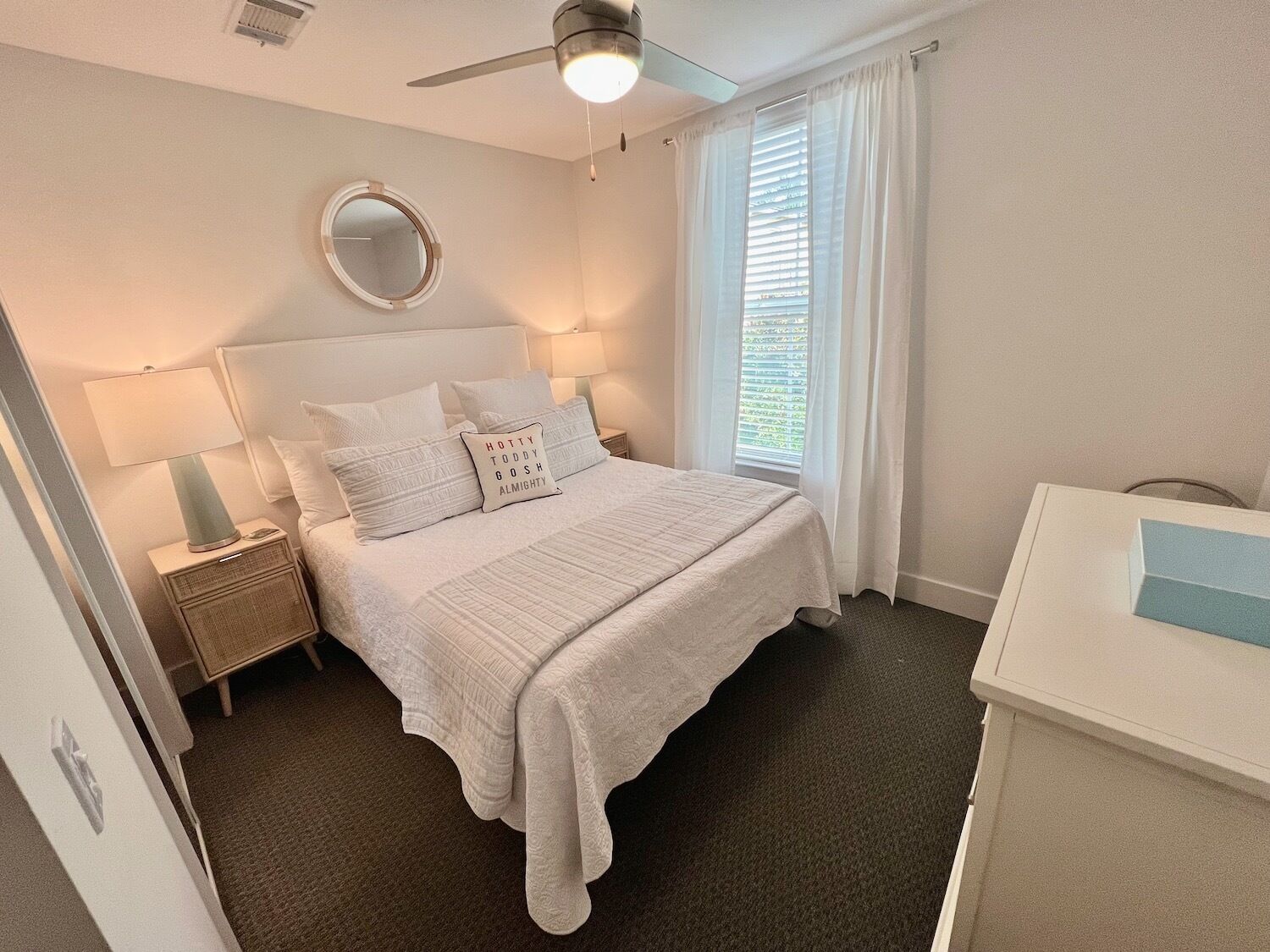 A neatly arranged bedroom with a bed, bedside tables, a mirror, and a window with curtains.