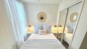 Ein ordentlich eingerichtetes Schlafzimmer mit Bett, Nachttischlampen, einem Spiegel und einem Kissen mit dem Wort "REBELLS".