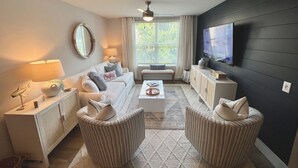 Ein modernes Wohnzimmer mit einer Couch, zwei Sesseln, einem Couchtisch, einem Fernseher und einem Kamin.