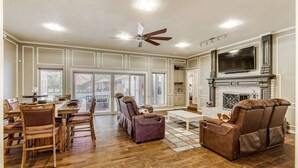 A spacious living room with a fireplace, a dining area with wooden chairs, and a ceiling fan. - Lake house with Hot tub 4 Bedroom and 3 Bath (Rowlett)