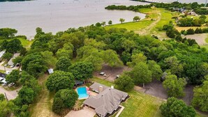 An aerial view of a residential area with a large body of water, a swimming pool, and a house with a fenced yard. - Lake house with Hot tub 4 Bedroom and 3 Bath (Rowlett)