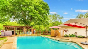A backyard with a swimming pool, a covered barbecue area, and a small building with a red umbrella. - Lake house with Hot tub 4 Bedroom and 3 Bath (Rowlett)