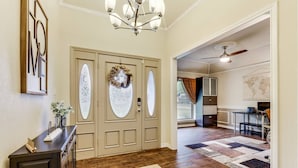 A hallway with a dark wooden floor, a beige door with a wreath, and a dark console table with a vase and a small plant. - Lake house with Hot tub 4 Bedroom and 3 Bath (Rowlett)