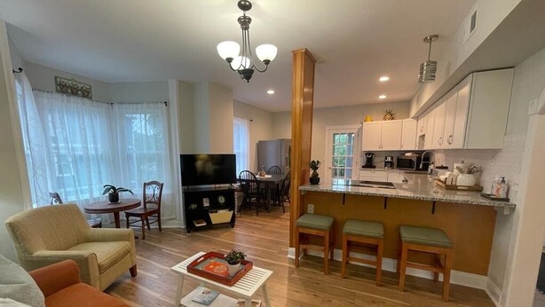 A modern living room with a sofa, coffee table, and TV. It includes a dining area with chairs and a kitchen with a bar.