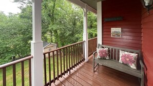 A wooden porch with a bench and a railing, surrounded by greenery.
