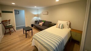 A bedroom with a bed, a sofa, a chair, a small table, and a nightstand.