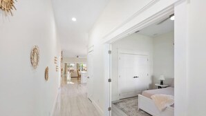 A hallway leading to a bedroom with a bed, a nightstand, and a lamp. There is a door on the right and a closet on the left. - New*Mini-Golf*Heat or Chill Saltwater Pool*Arcade (Jensen Beach)