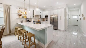 A modern kitchen with white cabinets, a large island with stools, stainless steel appliances, and pendant lighting. - New*Mini-Golf*Heat or Chill Saltwater Pool*Arcade (Jensen Beach)