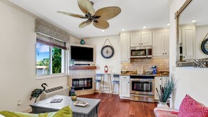 Una cocina moderna con armarios blancos, horno empotrado y microondas. Hay un comedor con mesa y sillas, y una sala de estar con sofá y televisor.