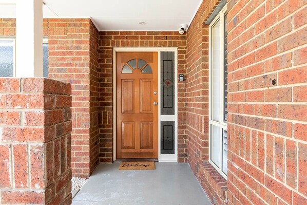 A brick house with a wooden front door, a welcome mat, and a small window. - Family Beach Getaway (Rosebud)