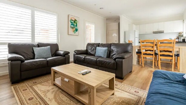 Een moderne woonkamer met twee leren banken, een houten salontafel en een eetgedeelte met houten stoelen.