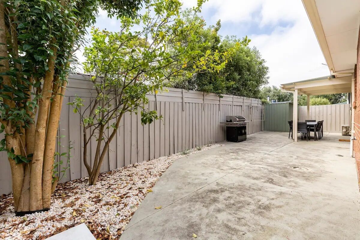 A backyard with a concrete patio, a barbecue grill, and a table with chairs.