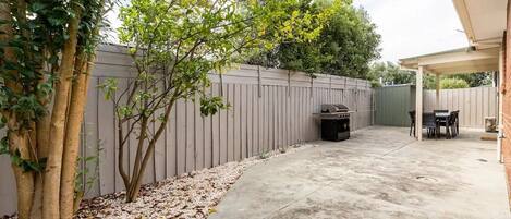 A backyard with a concrete patio, a barbecue grill, and a table with chairs.
