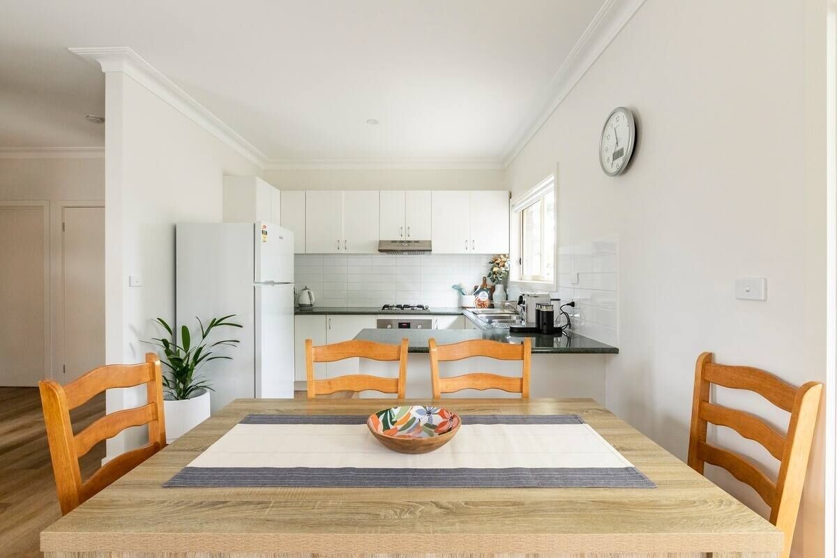 A modern kitchen with white cabinets, a refrigerator, and a dining area with a wooden table and chairs.