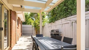 Een overdekt terras met een tafel, stoelen, een barbecue en een bakstenen muur.