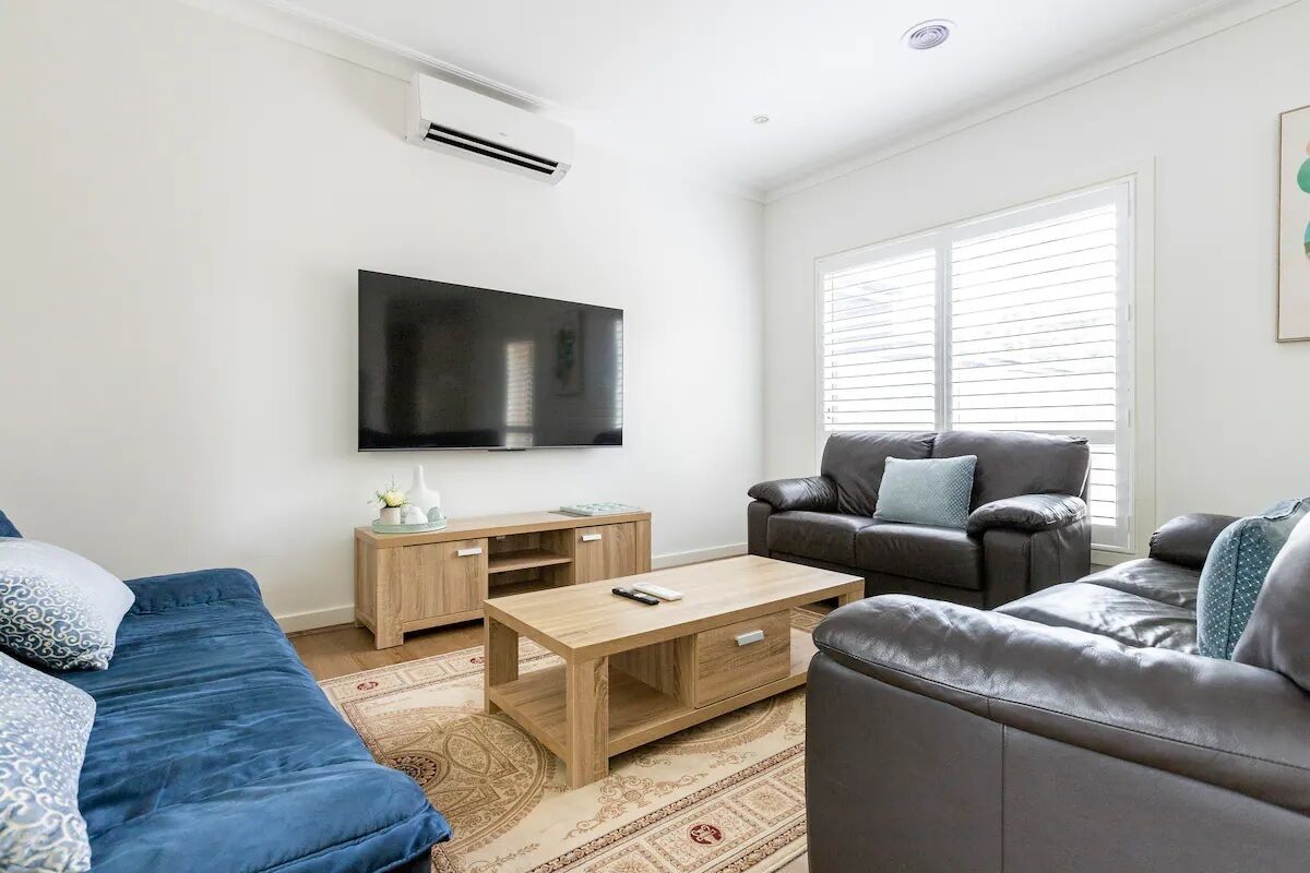 Una sala de estar moderna con un televisor de pantalla plana, una mesa de centro de madera, un sofá azul y un sofá de cuero.