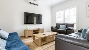 Een moderne woonkamer met een flatscreen televisie, een houten salontafel, een blauwe bank en een leren zithoek.