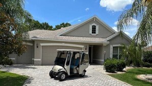 Une maison de plain-pied avec une allée pavée et un véhicule de golf garé devant.