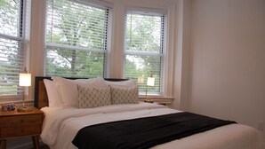 Ein Schlafzimmer mit einem Bett, einem Nachttisch mit Lampe und einem Fenster mit Jalousien.