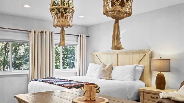 A hotel room with a large bed, a wooden nightstand, a table with a mug, and two hanging light fixtures. - 20% Off Valentines Studio at Sundance Utah (Sundance)