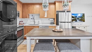 A modern kitchen with wooden cabinets, a stainless steel refrigerator, a microwave, and a sink. There are two hanging lights and a wooden dining table with two chairs. - 20% Off Valentines Studio at Sundance Utah (Sundance)