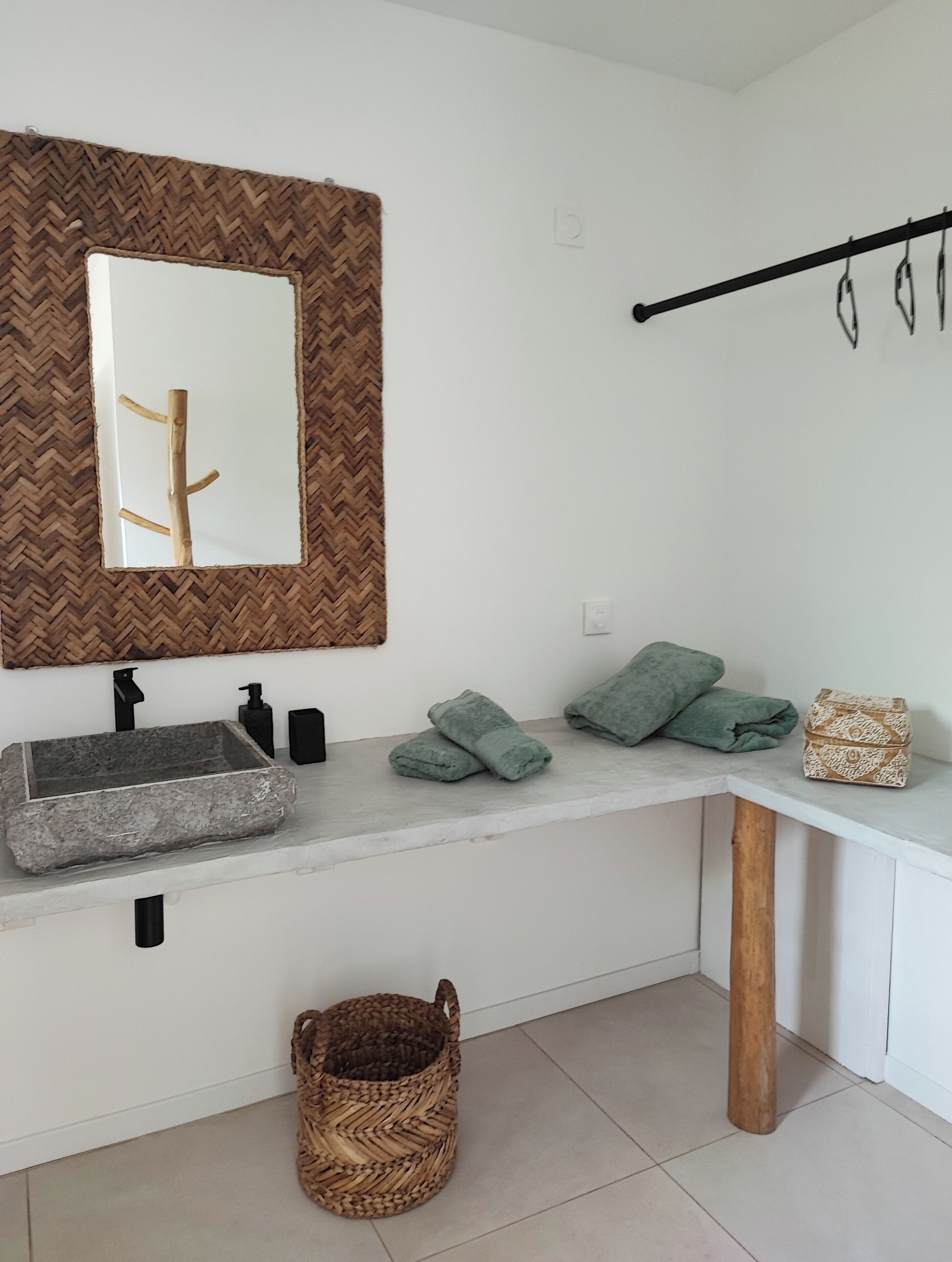 Un baño moderno con un lavabo de piedra, un espejo con marco tejido, un perchero y una cesta tejida.