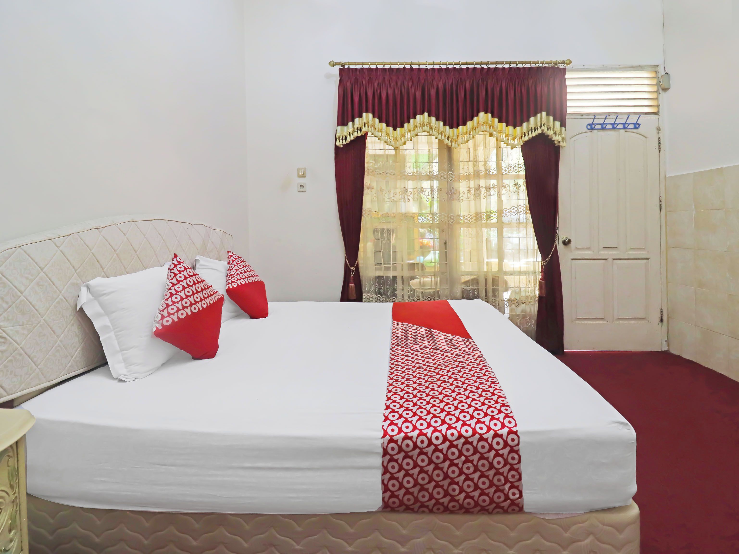 Una cama con cubrecama estampado, una ventana con cortinas y una puerta.