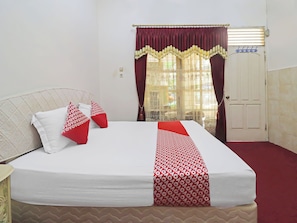 Un lit bien fait, recouvert d’une couette blanche et rouge, avec deux oreillers blancs et deux oreillers rouges à motifs.