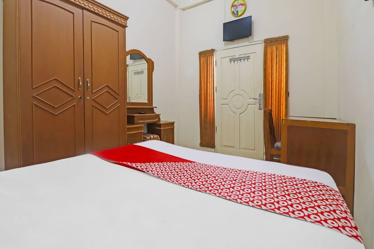 Un dormitorio con una cama grande, un armario, un escritorio, un espejo y un televisor en la pared.