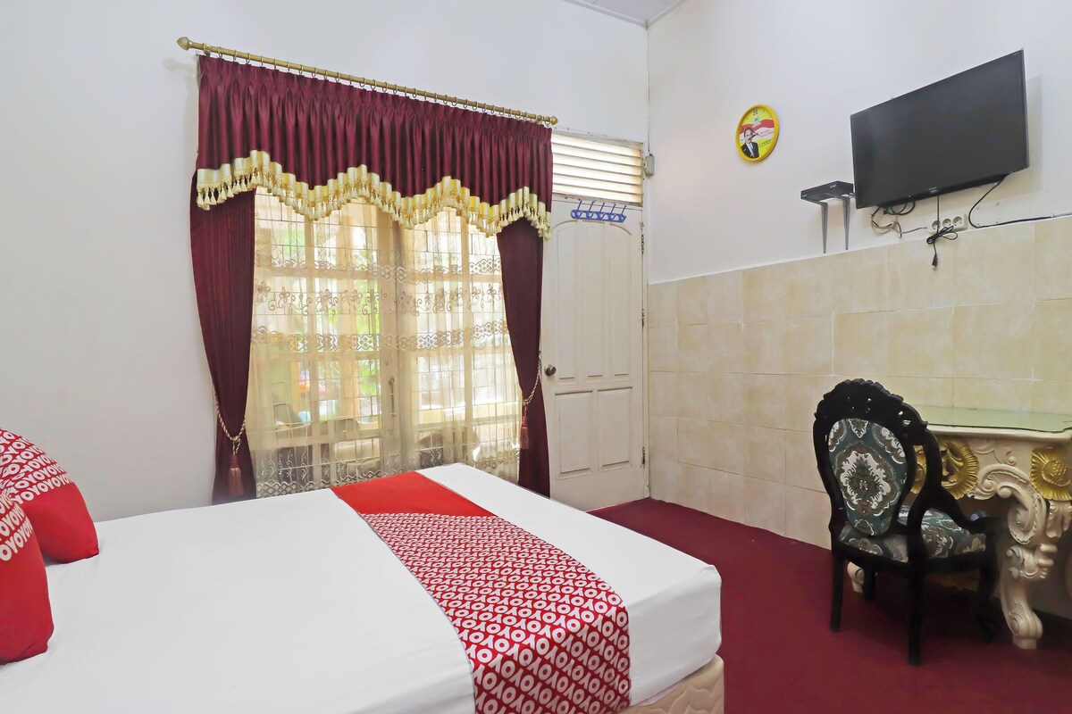 A hotel room with a bed, a desk, a chair, a TV, and a clock on the wall.