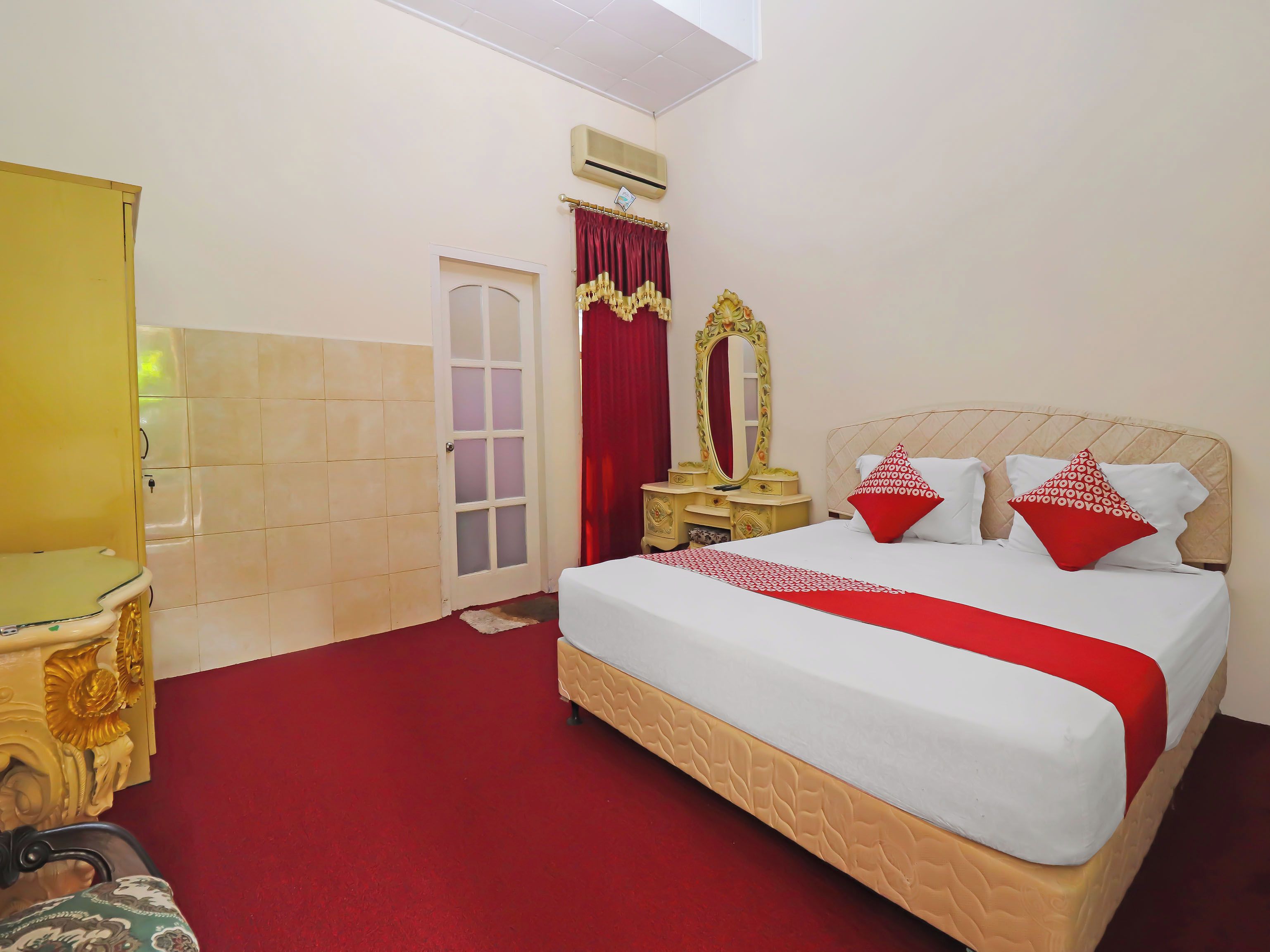 Una habitación de hotel con una cama, un tocador con espejo, una puerta y un equipo de aire acondicionado.