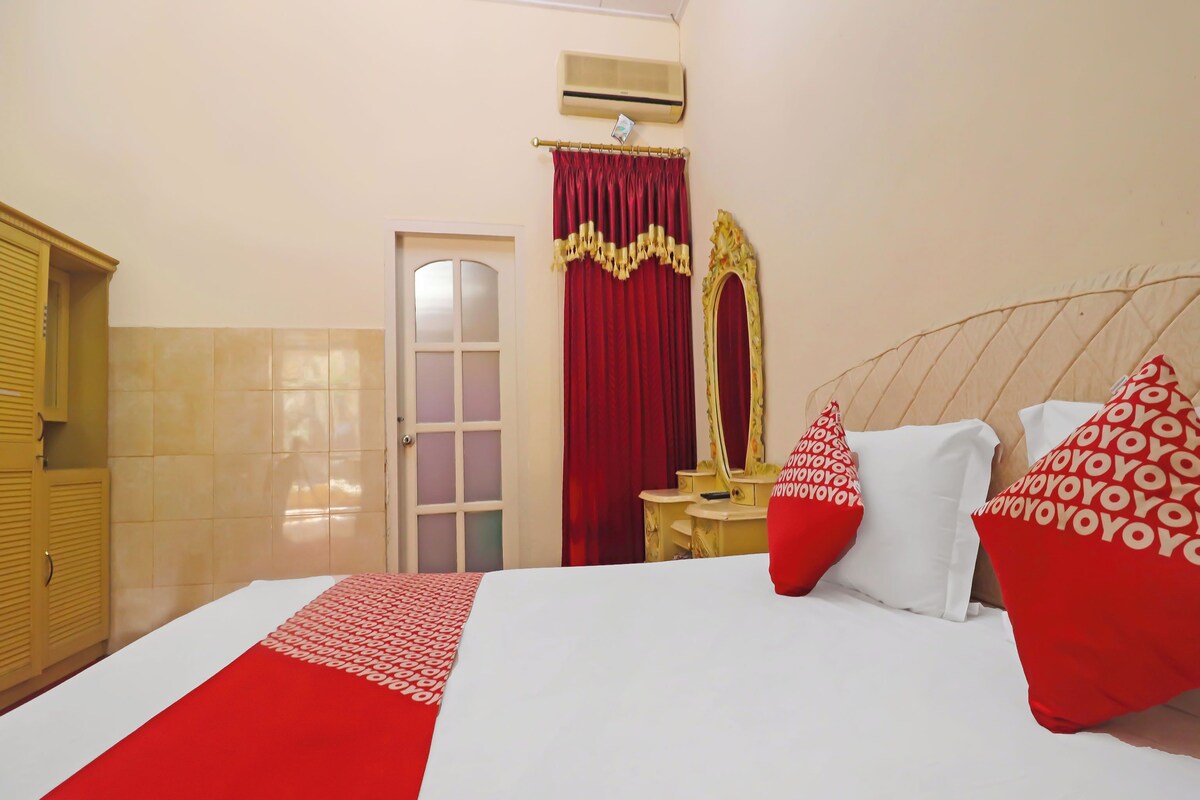 Ein Hotelzimmer mit einem Bett, einem Schminktisch mit Spiegel, einem roten Vorhang und einem rot-weißen Kissen.