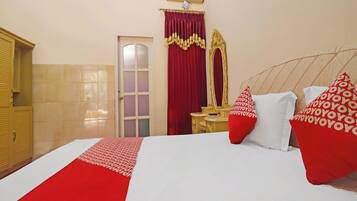 A hotel room with a bed, a vanity with a mirror, a red curtain, and a red and white pillow.