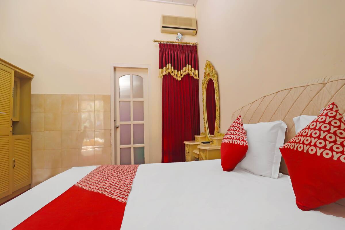 Una habitación de hotel con una cama grande, almohadas rojas y blancas, una tocador con espejo y una puerta con paneles de vidrio esmerilado.