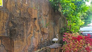 Een rustieke stenen muur met een vogelbeeldje, een klein bankje en potplanten.