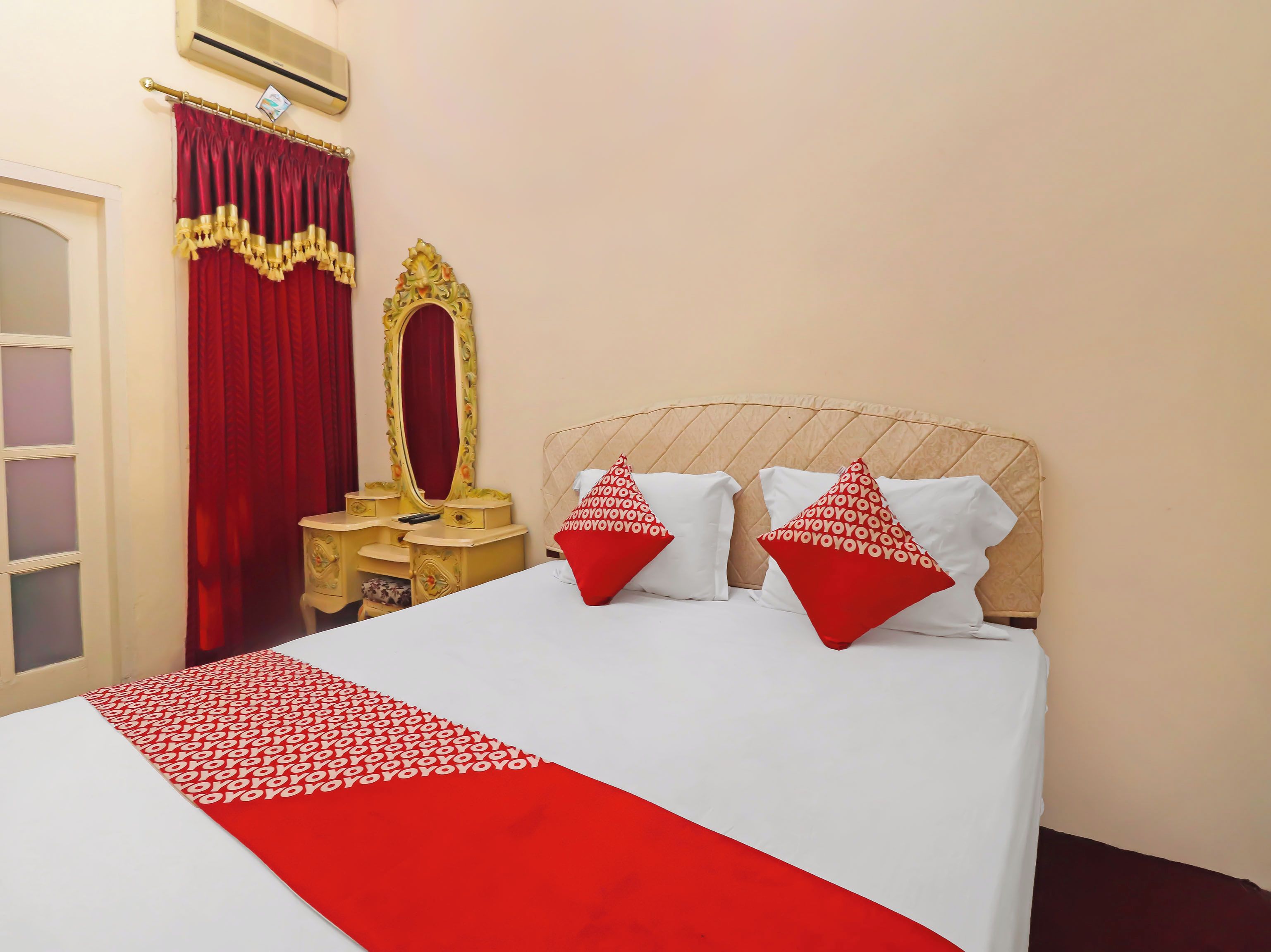 Una habitación de hotel con cama, tocador y espejo, y cortinas rojas.