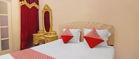 Una habitación de hotel con cama, tocador y espejo, y cortinas rojas.