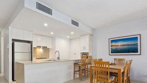 Een moderne keuken met witte kasten, een inbouweiland en een eethoek met houten stoelen en een tafel.