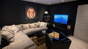 Uma sala de estar moderna com um sofá modular, uma mesa de centro, uma poltrona preta, uma televisão e uma estante de livros.