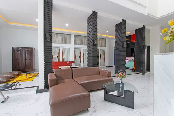 A modern living room with a brown sectional sofa, a glass coffee table, and a yellow rug. - Oyo 91665 D'prof Exclusive Guesthouse (Semarang)