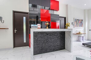 A reception area with a modern design, featuring a marble floor, a reception desk with a black and red decorative panel, and a wall-mounted phone. - Oyo 91665 D'prof Exclusive Guesthouse (Semarang)