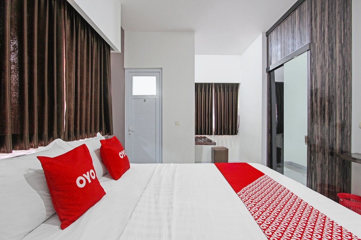 Habitación de hotel con una cama grande, una zona de estar pequeña, una puerta y una ventana con cortinas.