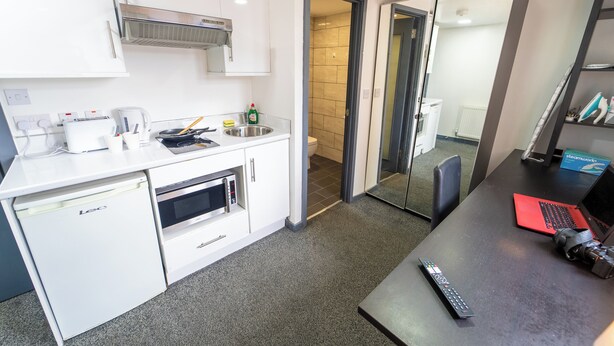 Een compacte keuken met een vaatwasser, magnetron en een klein aanrecht met waterkoker en afwasmiddel.