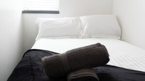 Een net opgemaakt bed met witte lakens en een opgerolde handdoek aan de zijkant.