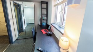 Een kleine kamer met een bureau, laptop en lamp.