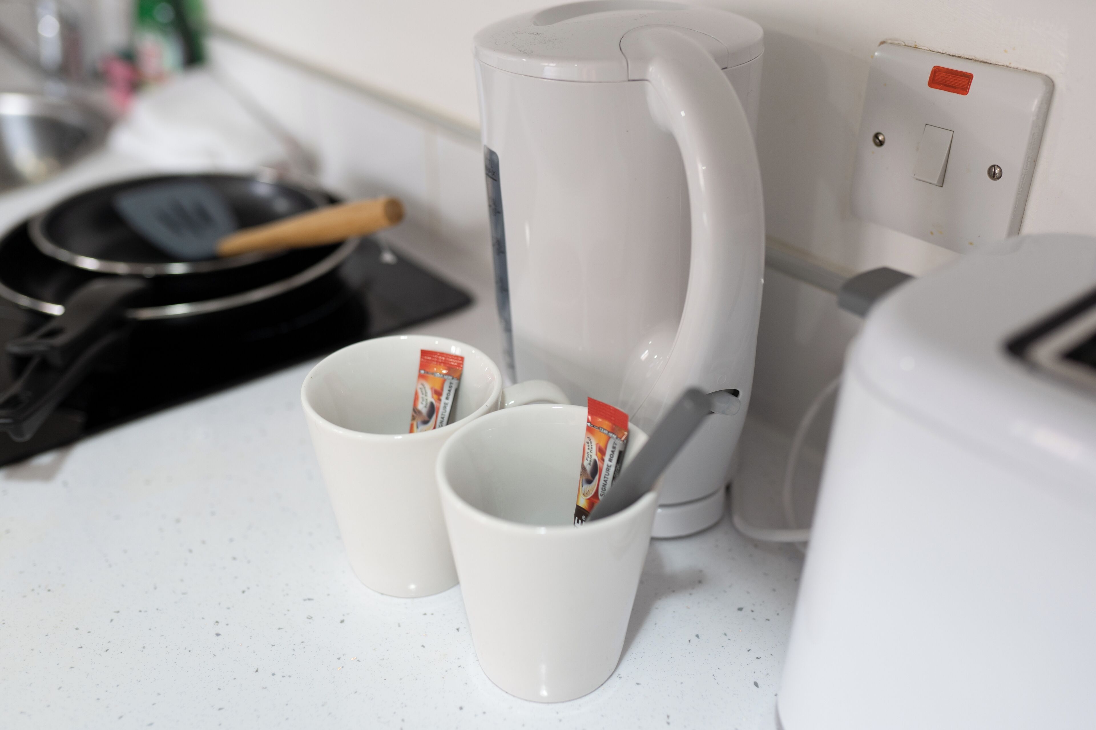 Un angolo cottura con una macchina da caffè, due tazze bianche e una padella.