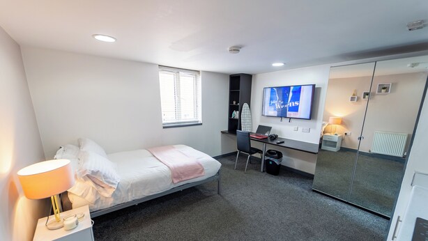 Een moderne hotelkamer met een eenpersoonsbed, een bureau met een laptop, een televisie en een kledingkast.